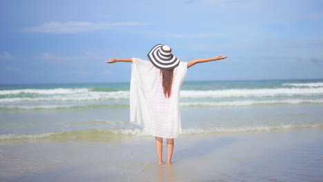 Espalda-De-Una-Mujer-Alegre-Con-Túnica-Blanca-En-La-Playa-De-Arena-Levantando-Los-Brazos-Frente-A-Las-Olas-Del-Mar-Y-El-Horizonte