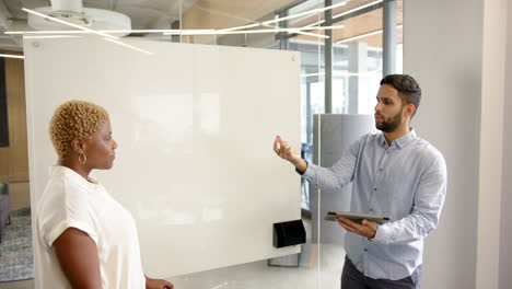 discussing project details, diverse colleagues using tablet and whiteboard in modern office