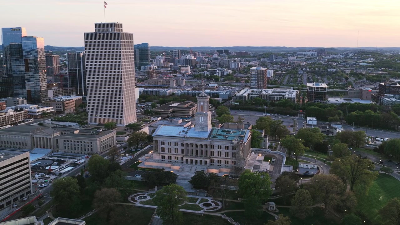 Dronebillede af Nashvilles Tennessee State Capitol og Metro Courthouse i skumringen, med et højt kontortårn, formelle haver og byens skyline i baggrunden.