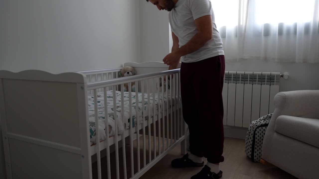 Dad looking at the baby crib in the room placing a stuffed animal