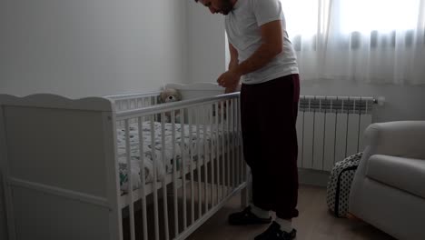 dad looking at the baby crib in the room placing a stuffed animal