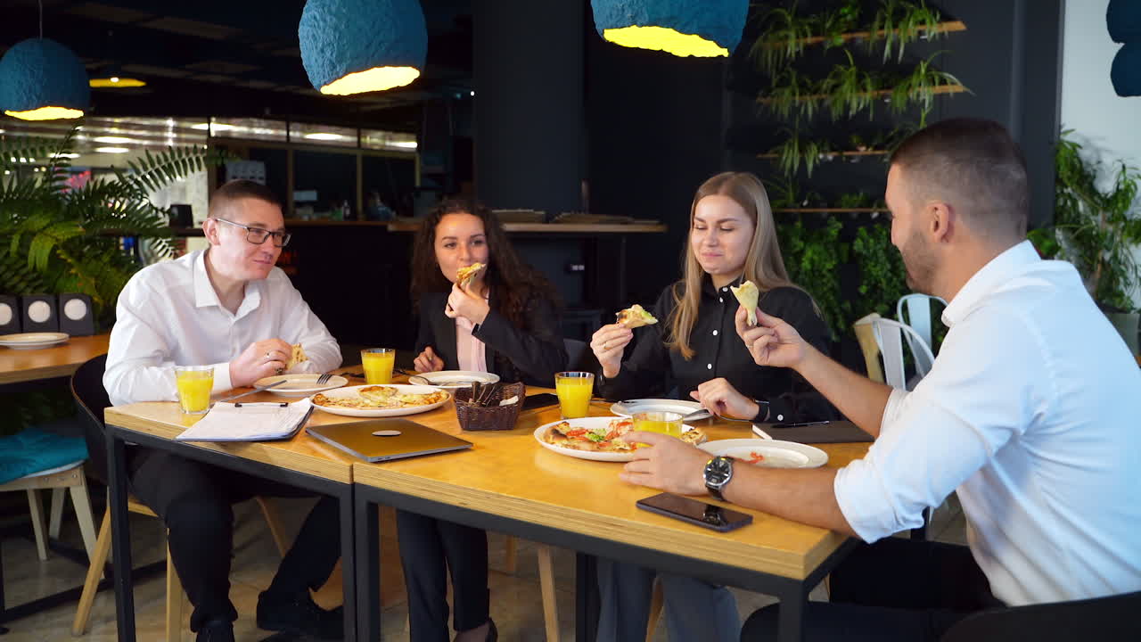 Office colleagues have lunch during break at work. Teammates enjoying pizza in a café at big table.