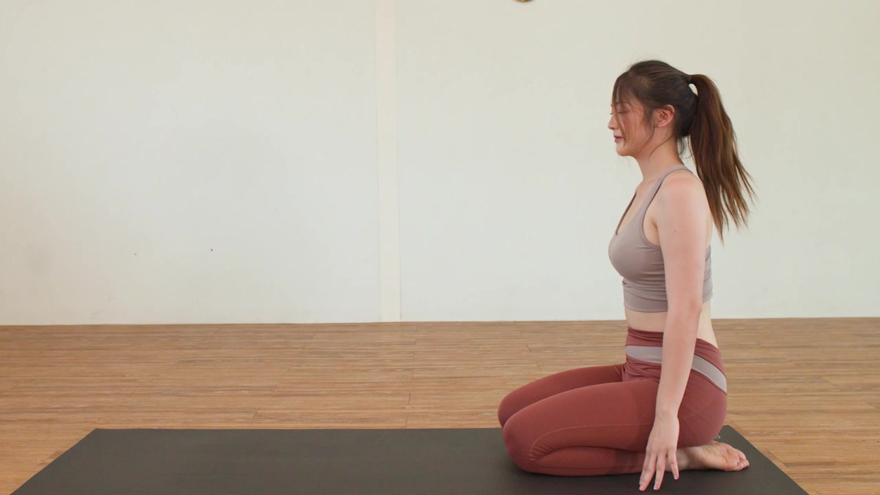 Young woman performs yoga transitions and leg stretches on a mat in a bright studio.
