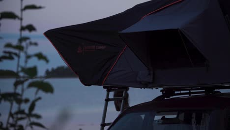 Tienda-De-Campaña-En-El-Techo-Del-Coche-Con-Un-Hombre-Durante-El-Campamento-Al-Aire-Libre-Al-Atardecer