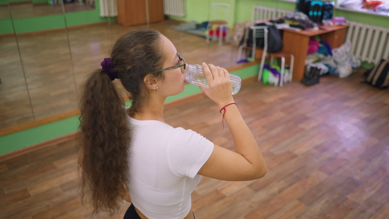 Girl standing with blurred background showing table chair cloth drinking water feeling relaxed calm healthy lifestyle wellness hydration balance peaceful refreshment modern indoor scene comfort