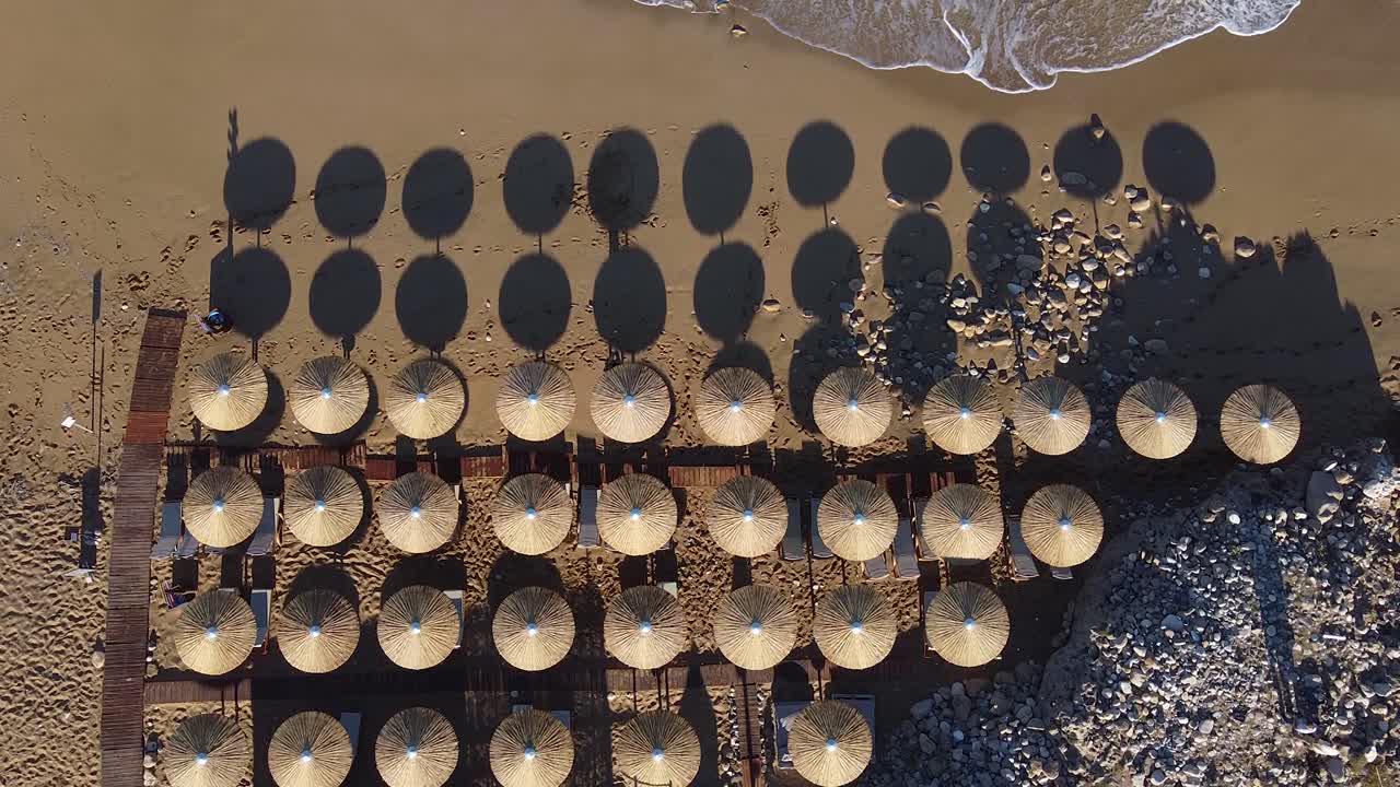 Aerial view looking down on an empty tropical beach with rows of empty beach umbrellas