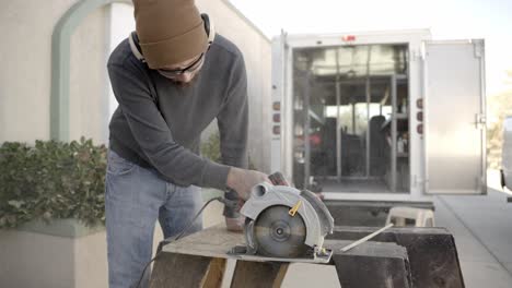 Man-cutting-wood-plank-with-hand-held-circular-saw-wide-shot-slow-motion