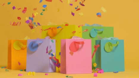 studio shot of colourful birthday party gift bags against yellow background with falling paper confetti 1