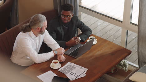 multiethnic businessmen using laptop and taking in cafe