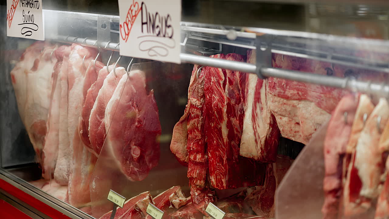 A display of meat in a store with a sign that says "Angus". The meat is hanging from hooks and it is fresh and red. Prime meet cut in butchery supermarket