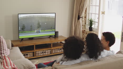 Compuesto-De-Familia-Feliz-Sentados-Juntos-En-Casa-Viendo-Un-Evento-De-Atletismo-De-Jabalina-En-La-Televisión