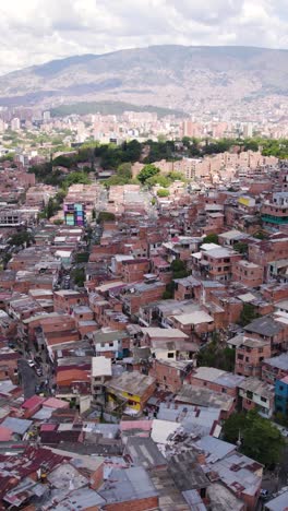 urban aerial view of comuna 13, a neighborhood known for its colorful houses, street art, and outdoor escalators, with the andes mountains in the background. vertical video