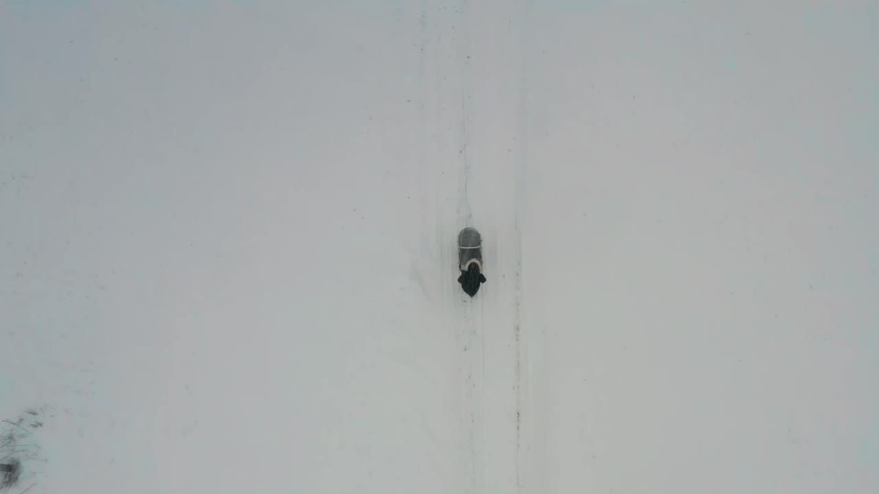 vista aérea de la madre empujando el carruaje del bebé en una carretera nevada mientras nieva