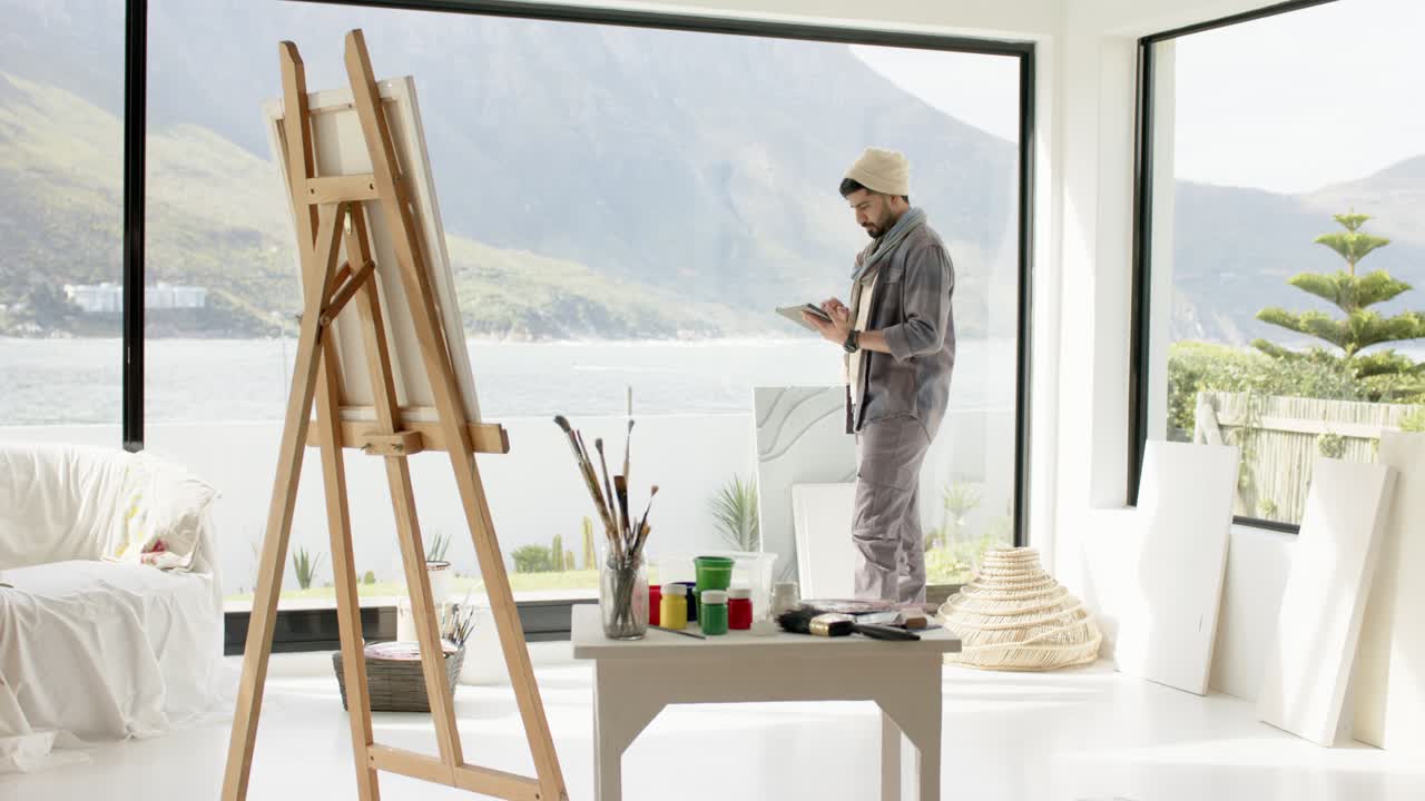 Indian man entering studio planning painting with sketchpad and stylus, sketching view, copy space