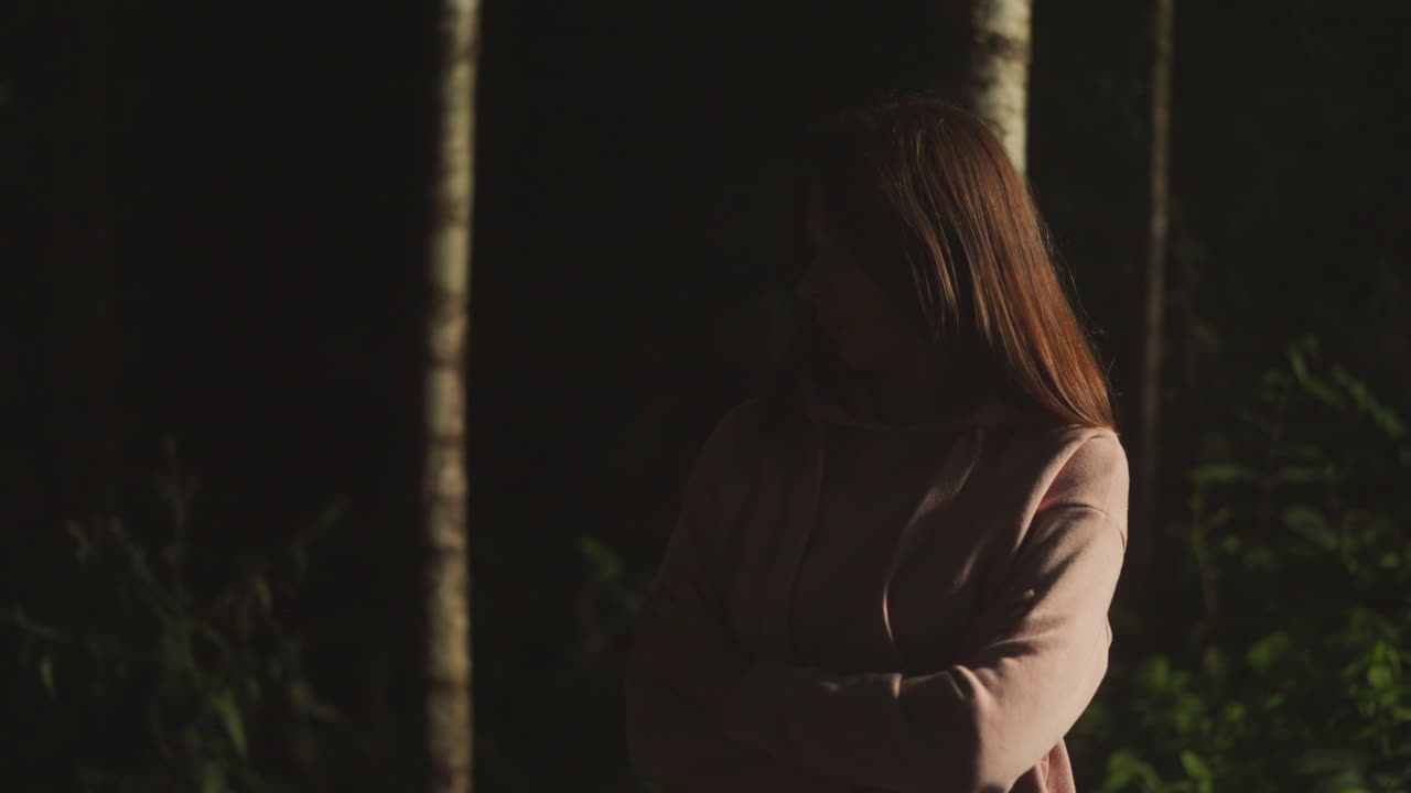 따뜻한 분홍색 코트를 입은 우울한 젊은 여성은 어두운 숲으로 사려 깊게 쳐다보고 있습니다. 여자는 문제를 생각하고 더 가운 자연을 즐기면서 과거를 기억합니다.