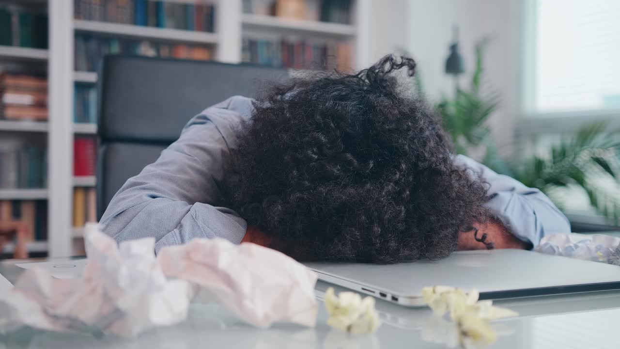 Young arabian man puts head on table with laptop and crumpled papers in office