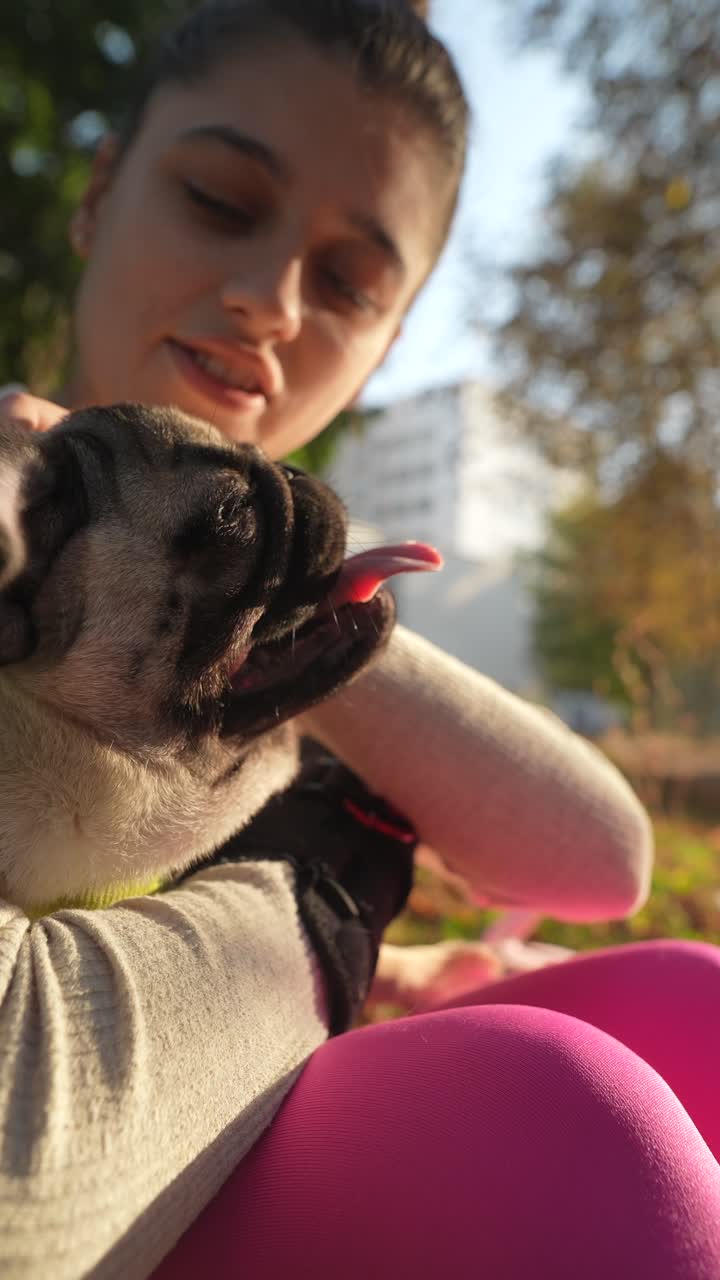 una mujer acurrucando a un pug en un parque.
