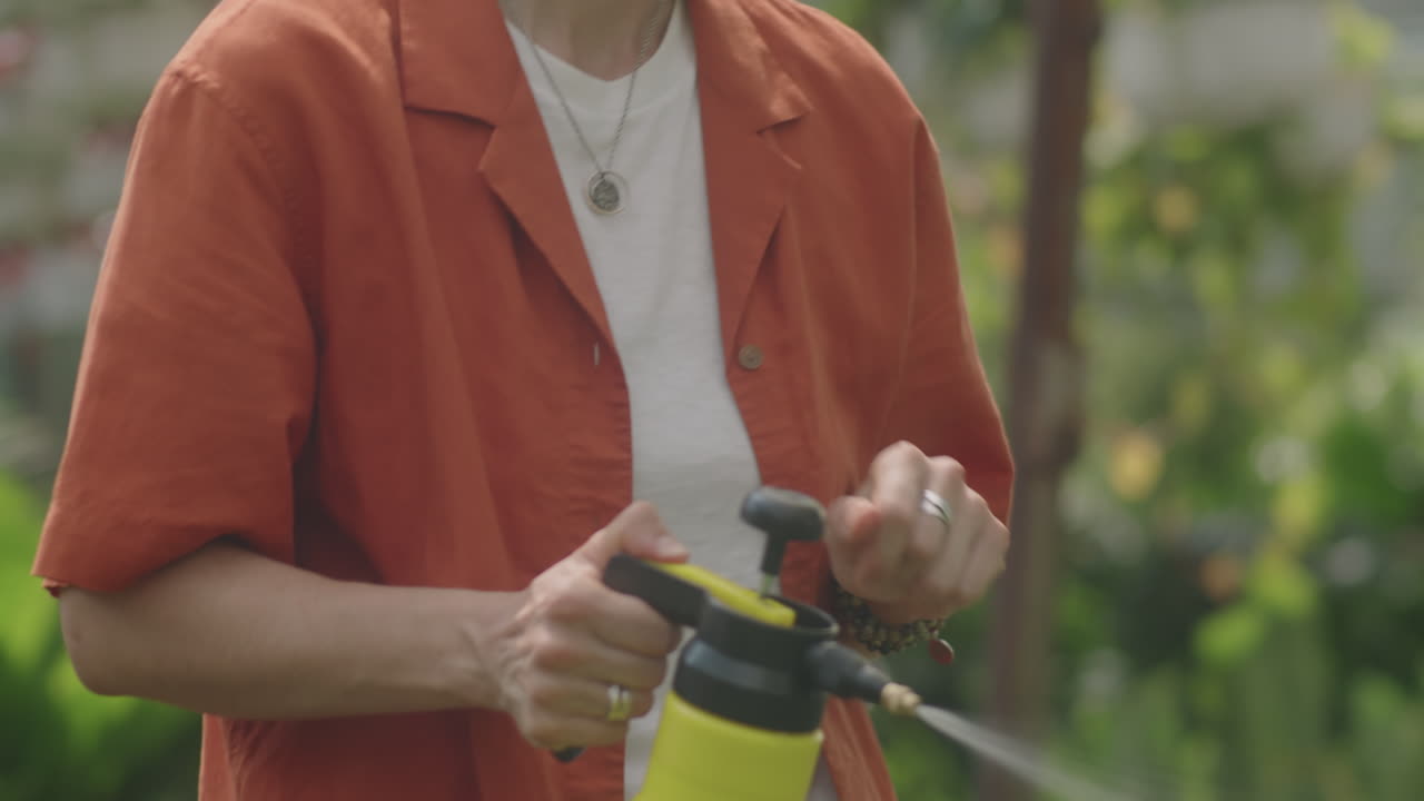Female Plant Nursery Worker Watering Flowers