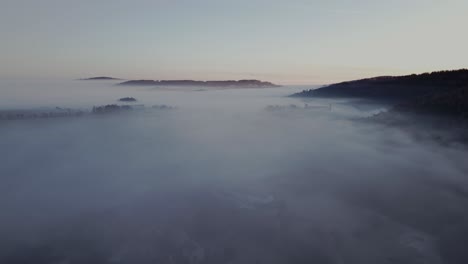 Vista-Aérea-De-Un-Paisaje-Místico-Y-Tranquilo-Envuelto-En-Una-Espesa-Niebla-Durante-El-Amanecer