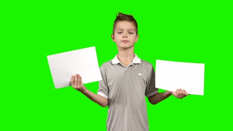 little boy holds two empty piece of papers in hands at green background