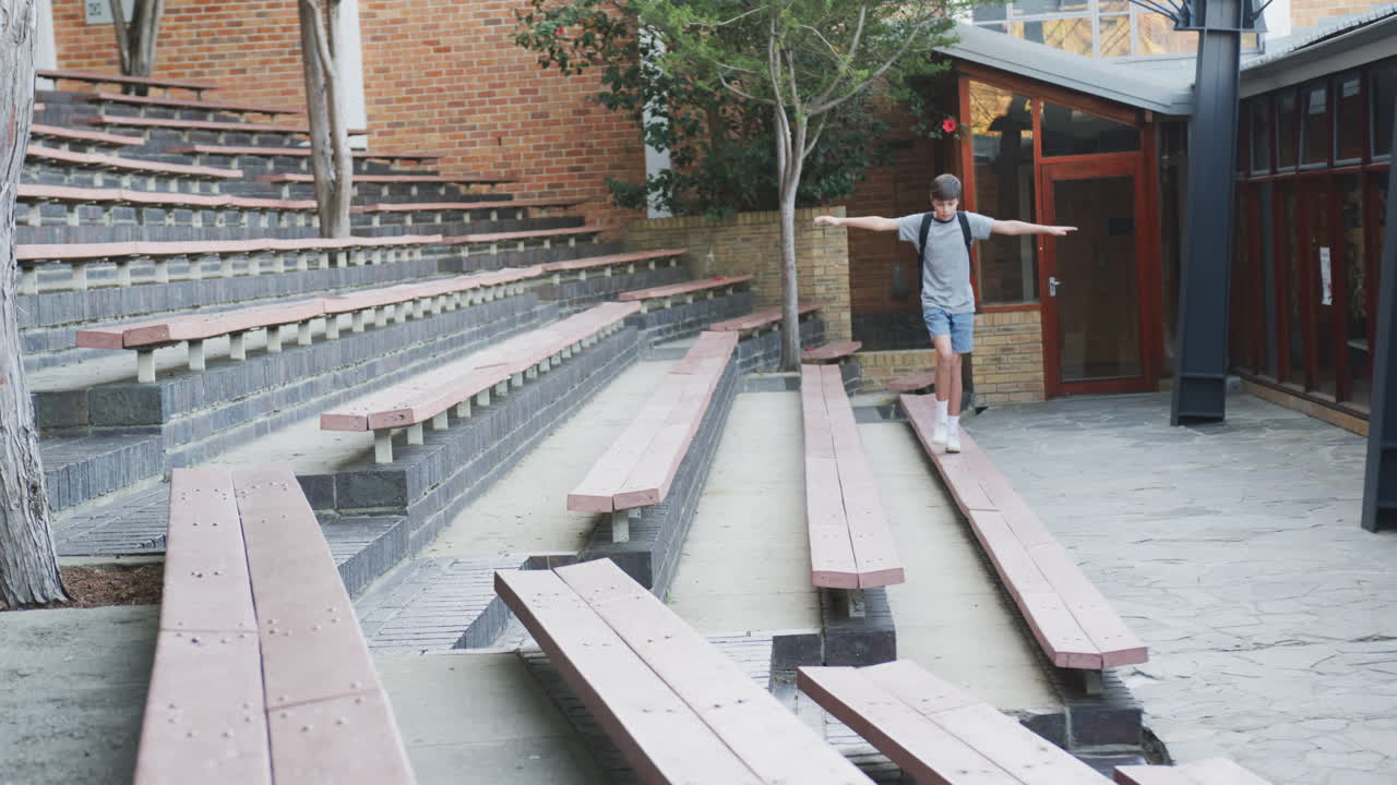 Balancing on bench, boy with backpack enjoying outdoor school amphitheater