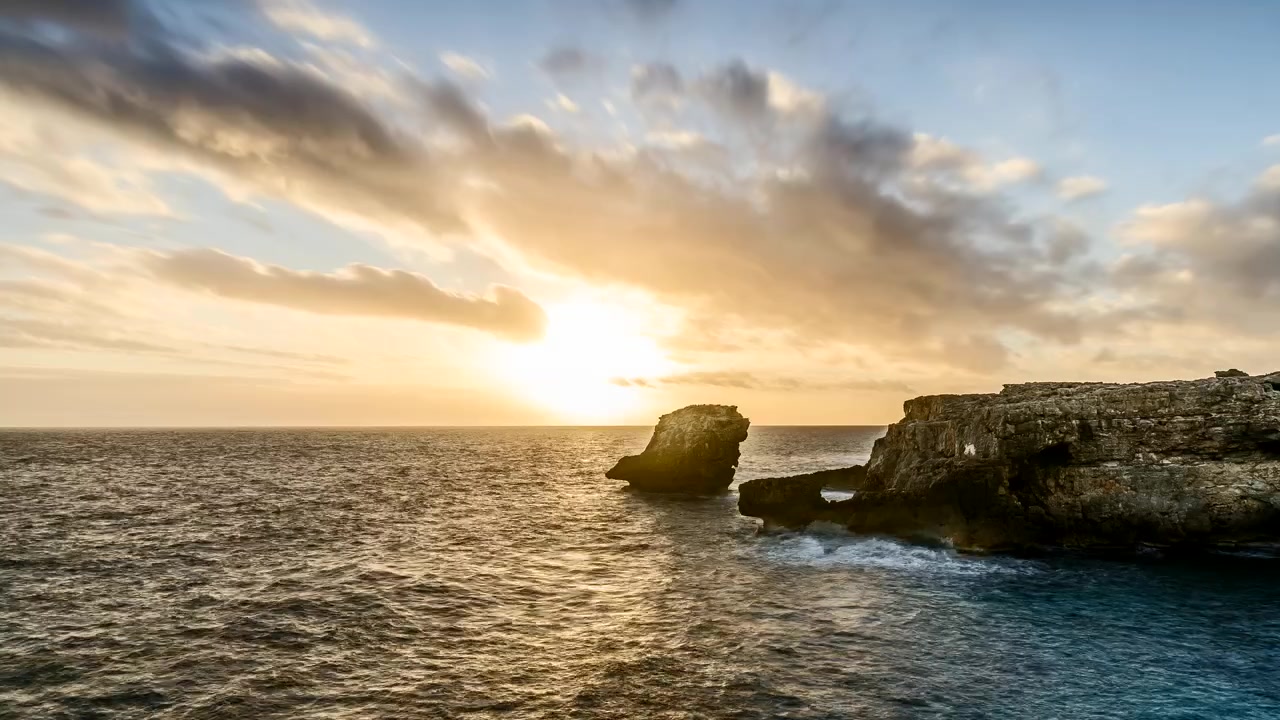 Um pôr do sol sobre a água e a costa rochosa da vila costeira de Binibeca. Time-lapse