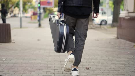 hombre camina por la calle sosteniendo un estuche de guitarra