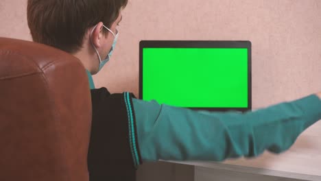 un hombre baila en una computadora en una videoconferencia en una máscara protectora, una tecla de croma en una pantalla de portátil y la alegría de un hombre