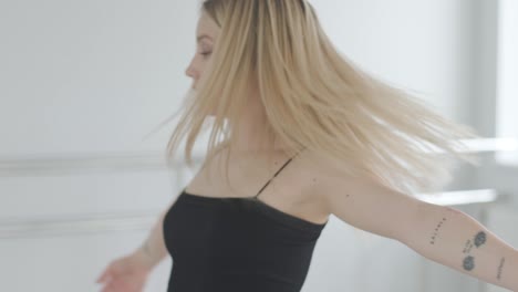 fit girl in black clothes performing contemporary. female dancer shows flowing motions, body and hands waves at white room. modern ballet dance choreography. young woman is moving smoothly