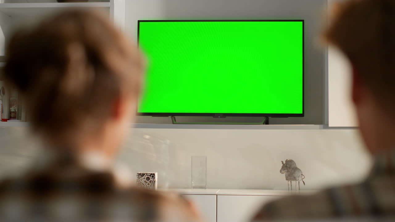 Friends playing green tv screen video game at home. Chroma key flat screen set.