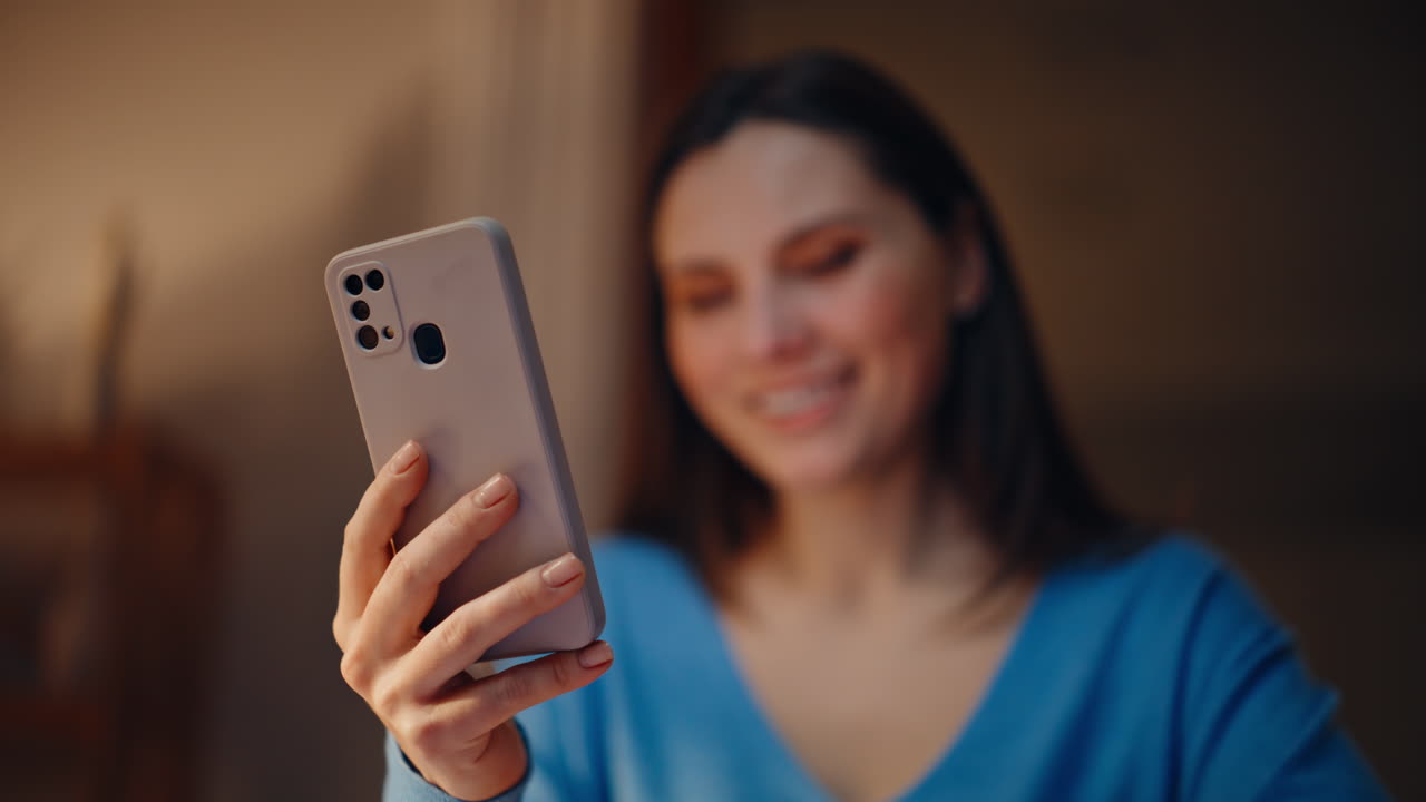 Brunette shopping online smartphone at dark apartment closeup. Smiling woman