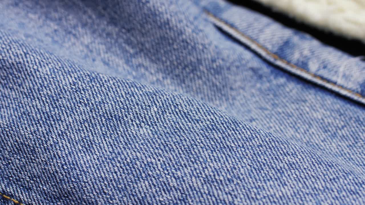 Panoramica macro su tessuto di jeans blu con cuciture a vista nell'inquadratura
