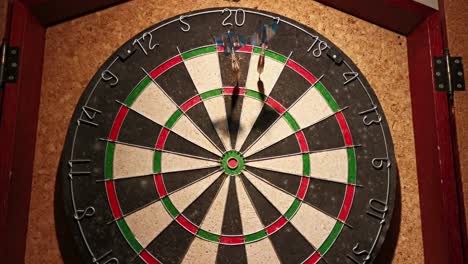 three darts hitting the top half of a dart board that hangs in front of a cork wall