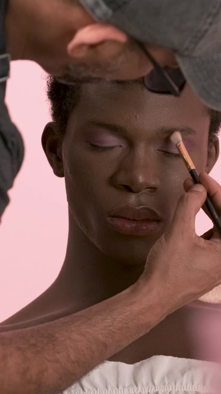 Crop visagiste doing professional makeup on transgender person. Vertical footage