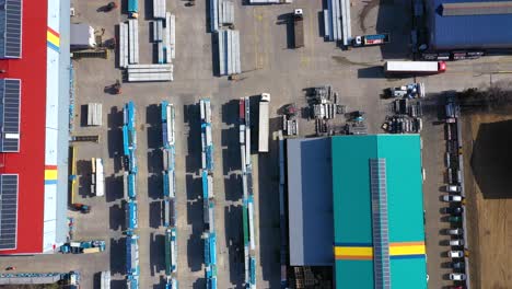 Aerial-view-of-a-semi-trucks-with-cargo-trailers-standing-on-warehouses-ramps-for-loading-unloading-goods-on-the-big-logistics-park-with-loading-hub