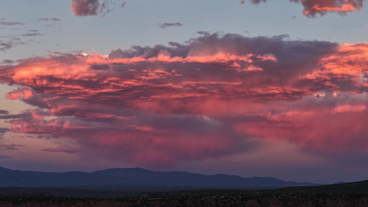 Timelapse 4K con drone di un clima mutevole del sud-ovest. La vibrante luce del tramonto cambia colore attraverso una massiccia formazione di nuvole lenticolari a forma di UFO che aleggia su un paesaggio montano scuro