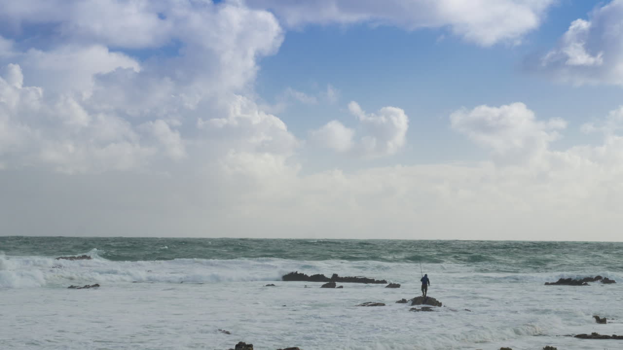 들어오는 조수에 갇힌 바위 해안선에서 낚시하는 남자