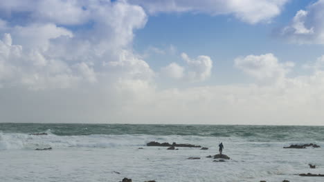 Man-fishing-on-rocky-coastline-trapped-by-incoming-tide