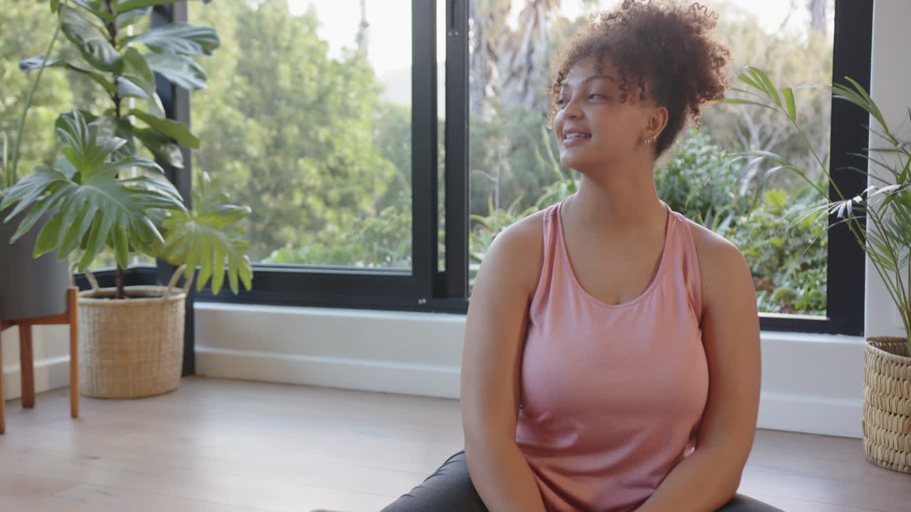 Smiling woman in workout clothes sitting on yoga mat in fitness studio, copy space