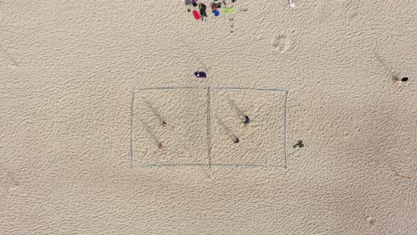 aerial: player serves volleyball to another person on sandy beach