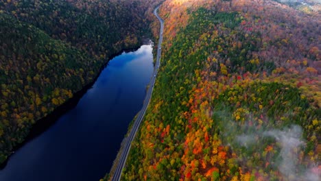 early morning aerial footage of a lake surrounded with fall colors in upstate new york showing a road as cars passing by