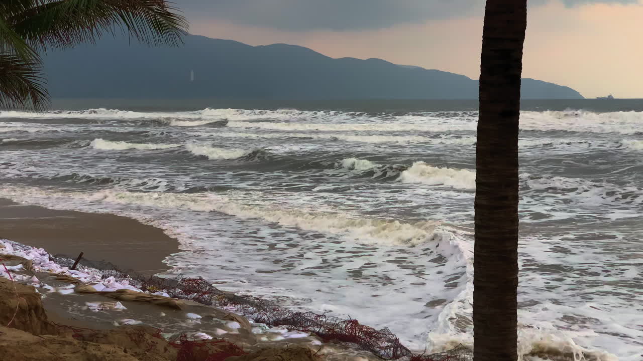 Turbulent beach in Da Nang, Vietnam, featuring crashing waves and the Son Tra Peninsula visible in the distance.