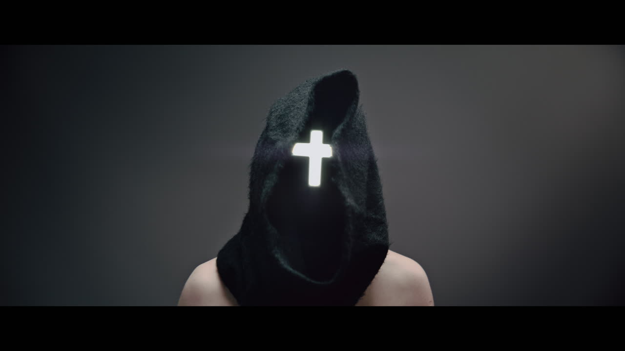 Masked and hooded man with cross of light glowing on his face rise his head