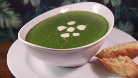 a bowl of green spinach soup with sliced garlic bread rotating with close up shot