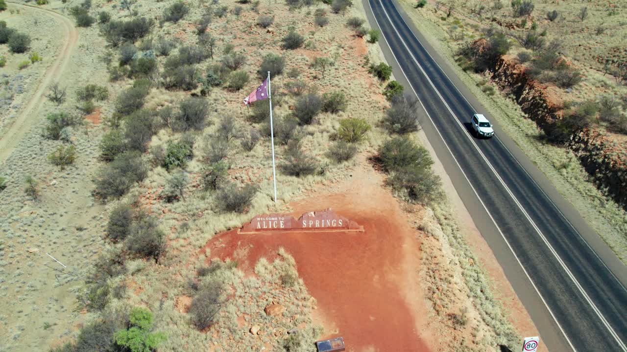 Zooming out drone view of the Alice Springs sign along the Stuart Highway, revealing the town of Alice Springs, Mparntwe, Northern Territory, Australia. August 2022.