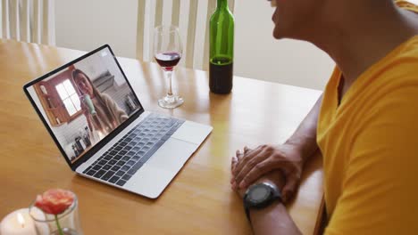 Mid-section-of-african-american-man-with-wine-having-a-video-call-on-laptop-at-home