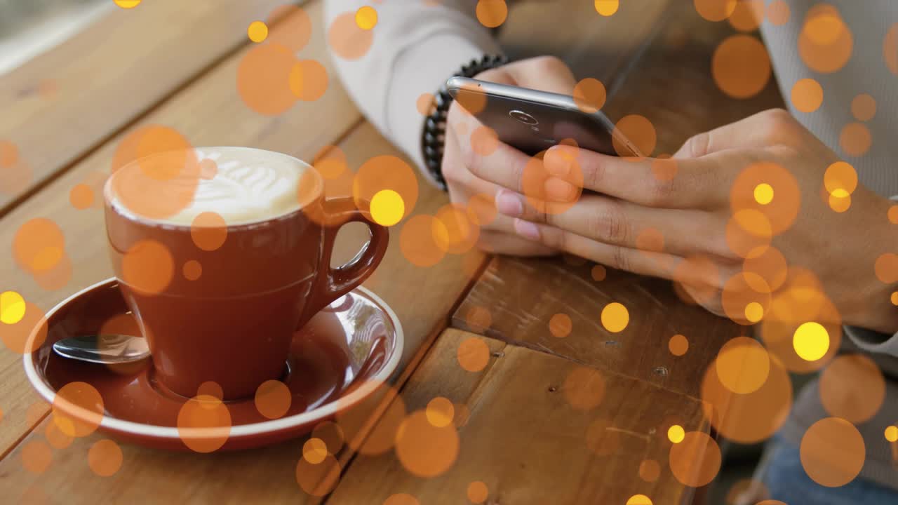 Hombre tocando el smartphone y desplazándose por un feed tecnológico con luces bokeh doradas flotando sobre un café con leche.