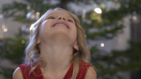 retrato de cara cercana de una niña feliz de cinco años junto al árbol de navidad decorado