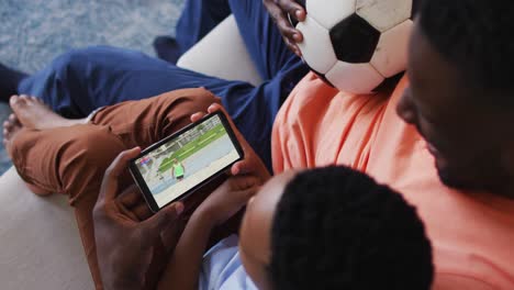 Compuesto-De-Padre-E-Hijo-En-Casa-Viendo-Un-Evento-De-Salto-De-Altura-De-Atletismo-En-Un-Teléfono-Inteligente