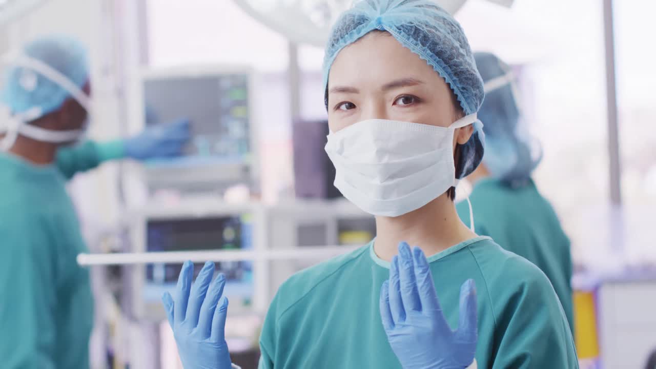 수술실에서 모자, 장갑 및 얼굴 마스크를 입은 아시아 여성 외과의사의 비디오 초상화, 복사 공간